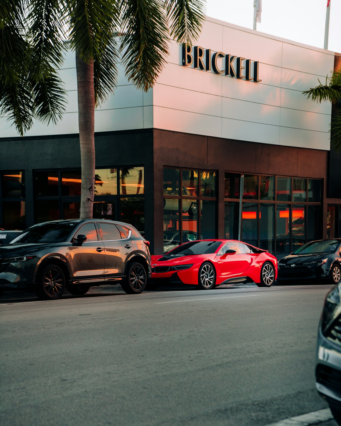 Modern cars parked on a city street at sunset.