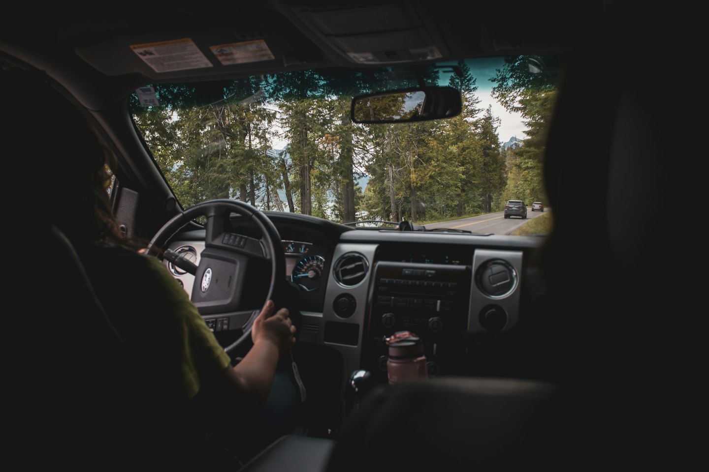 Hands gripping a steering wheel while driving on a winding road.